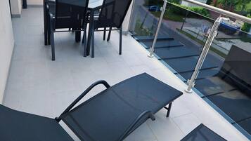 A rooftop terrace with a table and chairs, a glass balustrade, and a view of the surrounding area.
