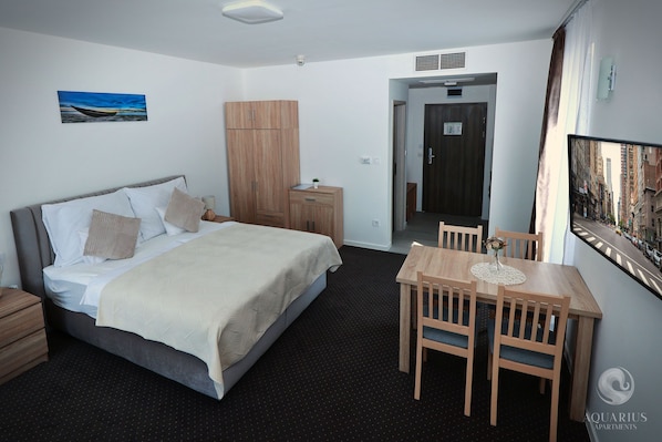 A hotel room with a bed, bedside table, wardrobe, and a dining area with chairs and a table.