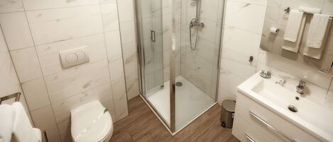 Un baño moderno con ducha envuelta en vidrio, inodoro blanco y tocador con espejo y lavabo.