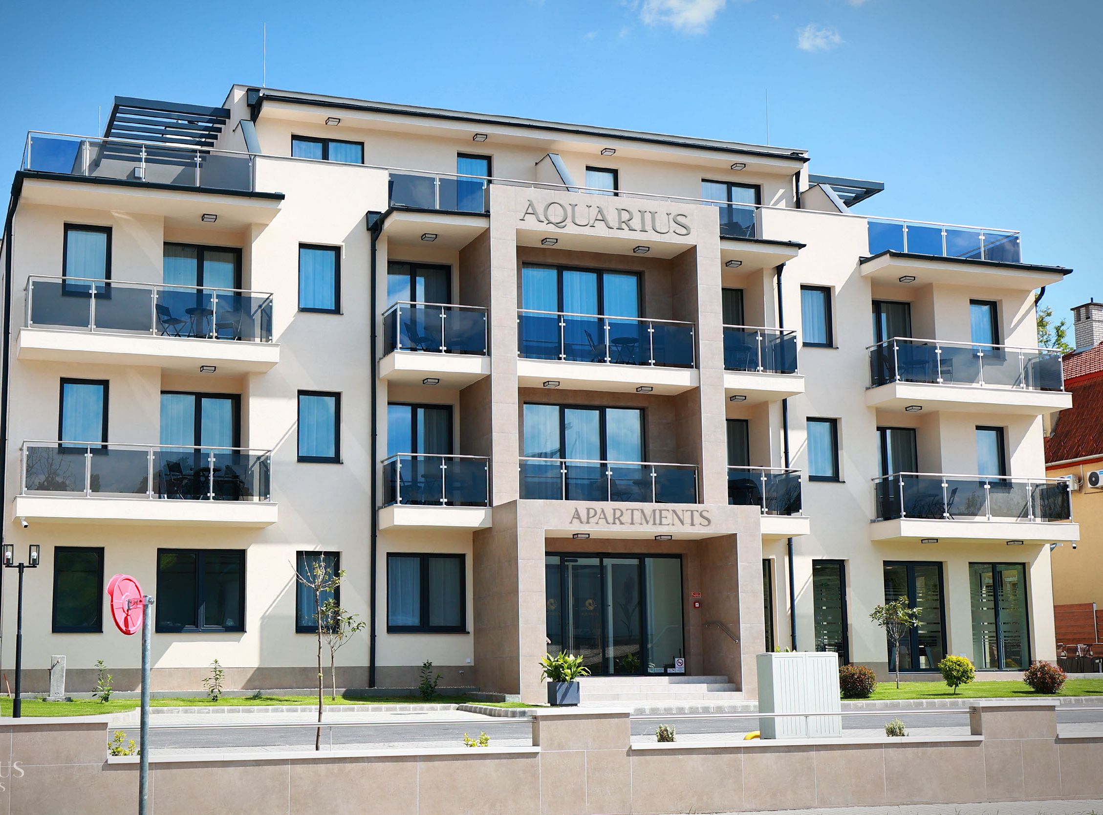 Ein mehrgeschossiges Gebäude mit Balkonen, mit der Aufschrift „AQUARIUS APARTMENTS“, das ein modernes architektonisches Design mit großen Fenstern und einem Flachdach aufweist.