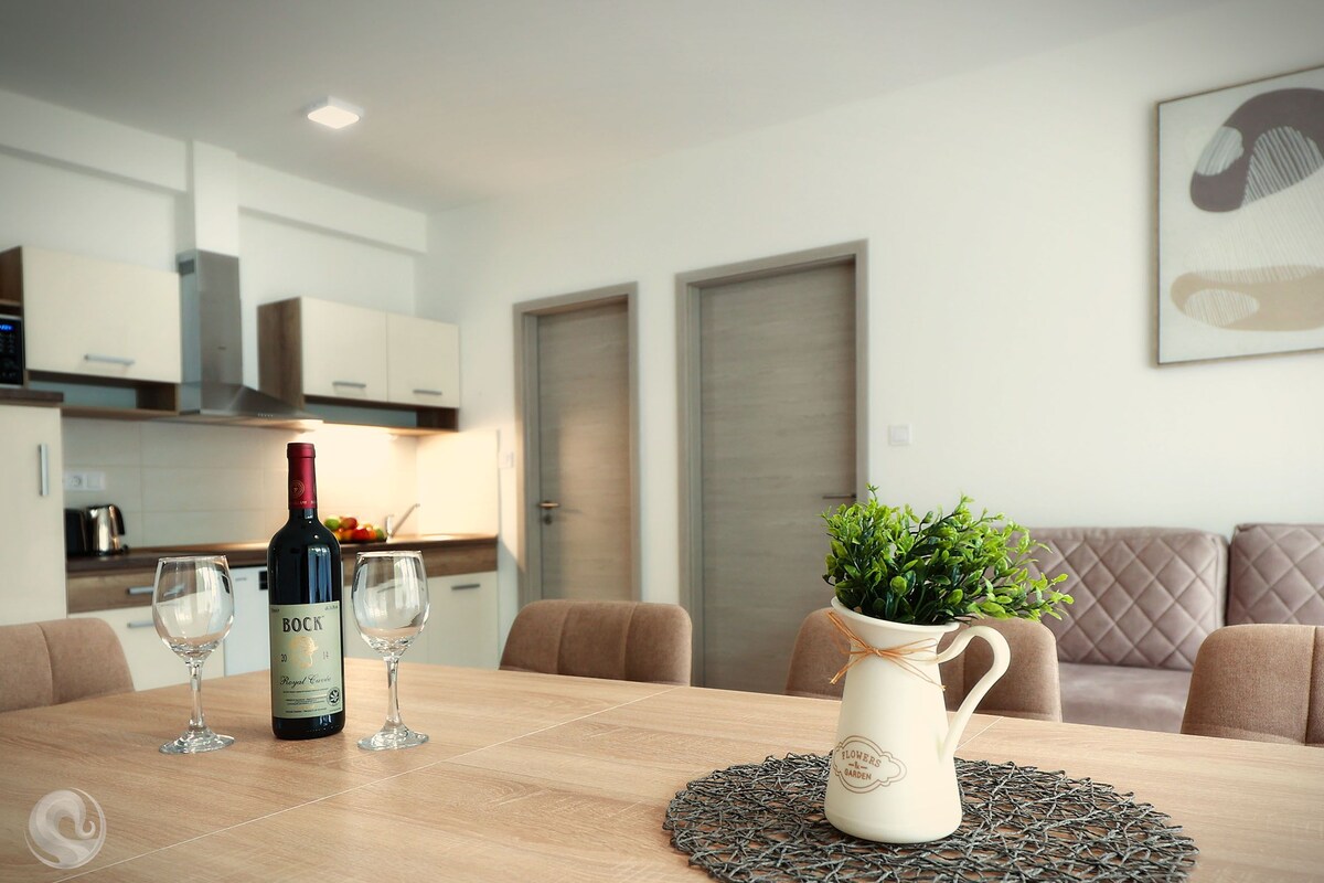 A dining table with a bottle of wine, two glasses, and a potted plant.