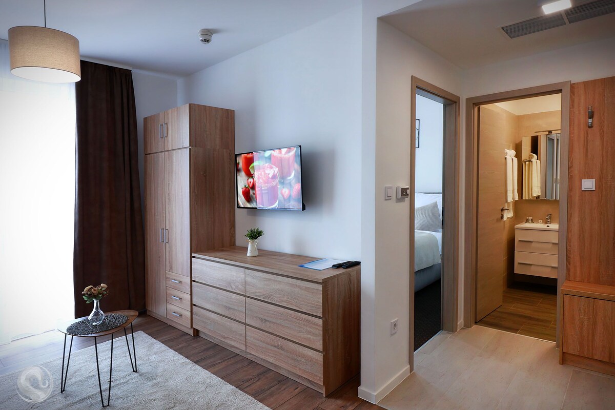 A modern bedroom with a wooden wardrobe, a TV mounted on the wall, and a small table with a vase.