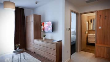 Ein modernes Schlafzimmer mit einem Holzschrank, einem an der Wand montierten Fernseher und einem kleinen Tisch mit einer Vase.