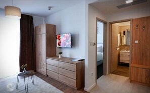A modern bedroom with a wooden wardrobe, a TV mounted on the wall, and a small table with a vase. - Aquarius Apartments (Miskolc)