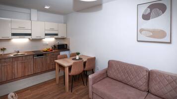 A modern kitchen with wooden cabinets, a dining area with a table and chairs, and a pink sofa in a living room.