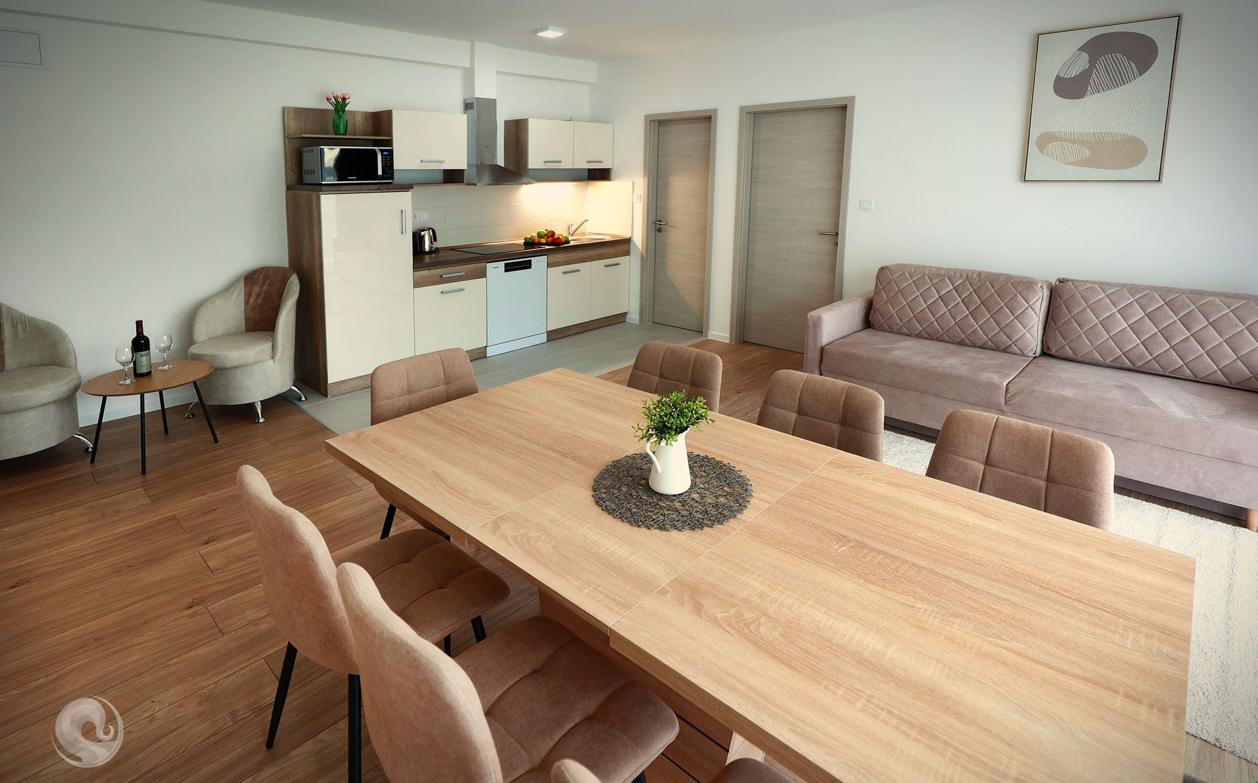 Una sala de estar moderna con una mesa de comedor de madera, sofás color beige y una cocina con armarios blancos y un microondas.