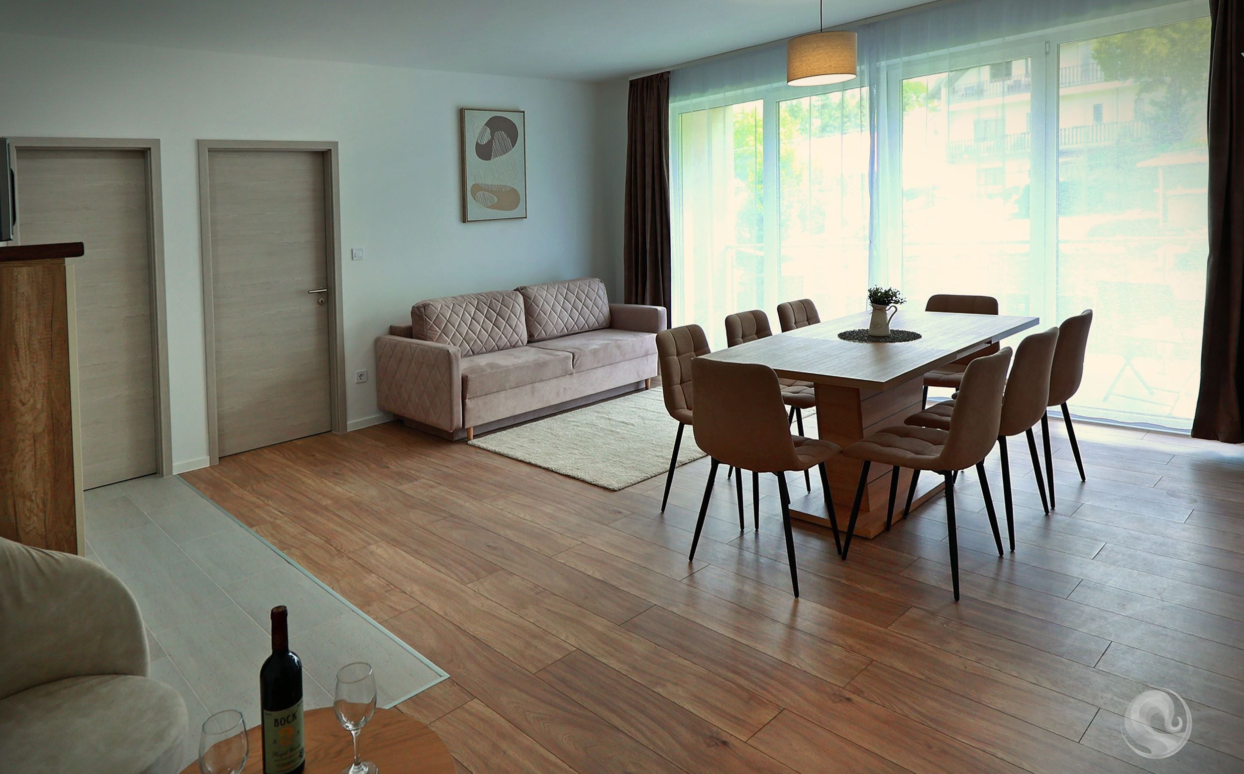 Una sala de estar moderna con piso de madera, un sofá color beige, una mesa de comedor con sillas y una botella de vino.