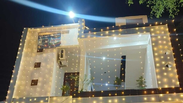 A modern two-story building with string lights, a gated entrance, and potted plants. - S K HOMESTAY (Tulapur)
