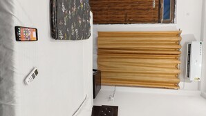 A bedroom with a bed, an air conditioner, a wooden wardrobe, a curtain, and a mobile phone on the bed. - S K HOMESTAY (Tulapur)