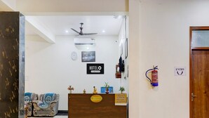 Zona de recepción de un hotel con mostrador, un reloj, unidad de aire acondicionado, extintor y un cartel que indica horarios de registro de entrada y salida.