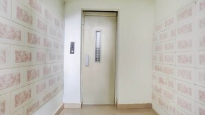 Un pasillo con una puerta que tiene un ventanal vertical y un panel de control.