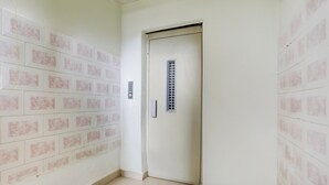 Un pasillo con pared de azulejos, una puerta con rejilla de ventilación e interruptor de luz.
