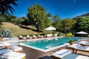 A pool area with lounge chairs and umbrellas, surrounded by trees and a hilly landscape. - Oasi Dolce Vita house surrounded by greenery with swimming pool, tennis and panoramic view (Lozzo Atestino)