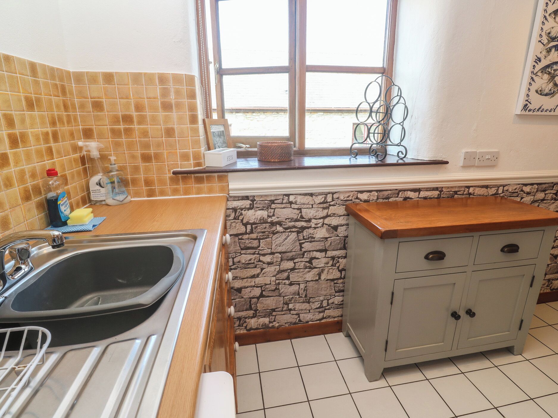 Eine Küche mit Steinrückwand, einer Holzausziehtafel, einem Spülbecken und einem Schrank mit Schubladen.