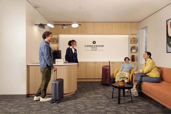 A hotel reception area with a reception desk, a sign for Candlewood Suites by IHG, and a seating area with a sofa and a small table.