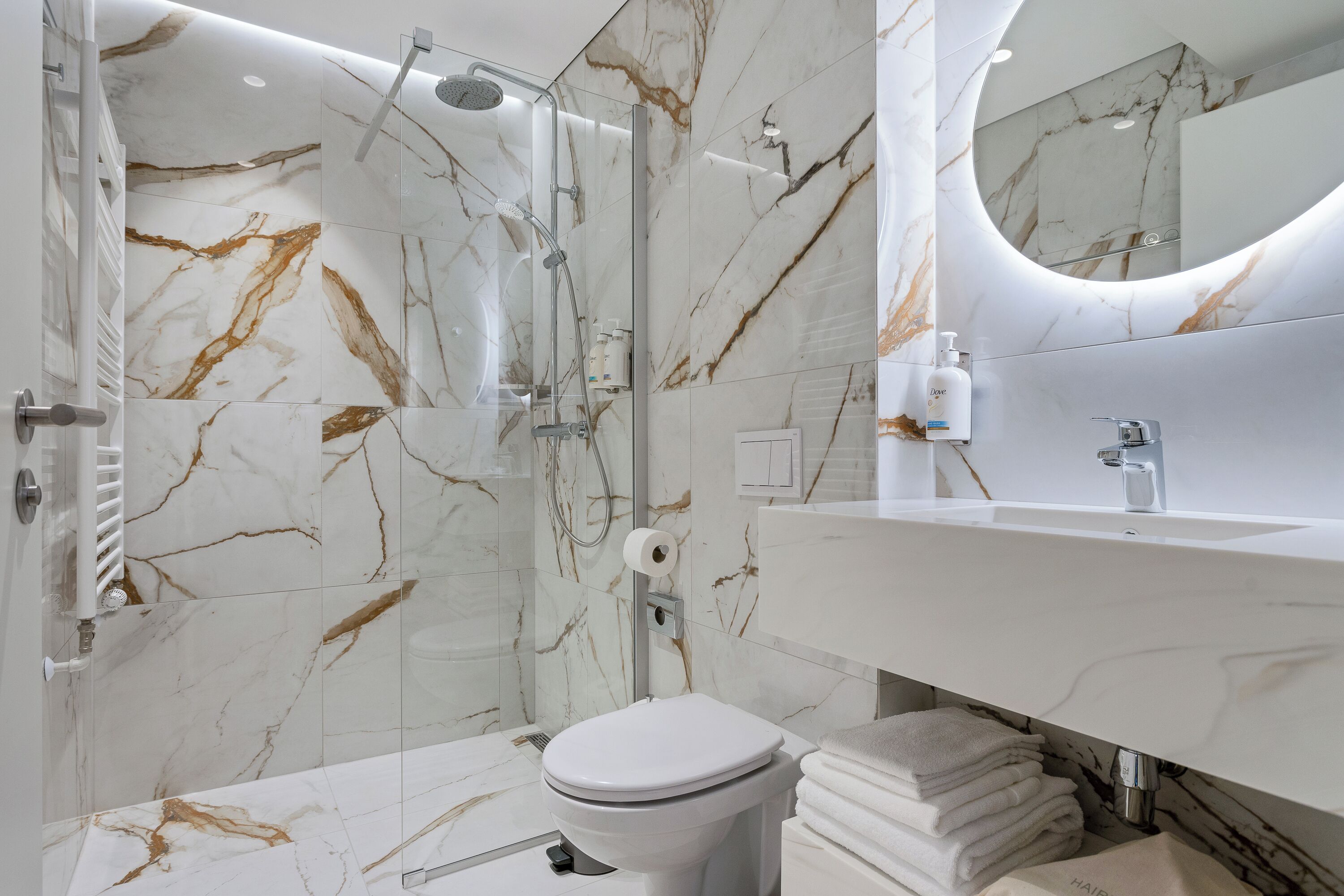 Un baño moderno con salpicadero de mármol, ducha con cerramiento de vidrio, lavamanos blanco y un inodoro.