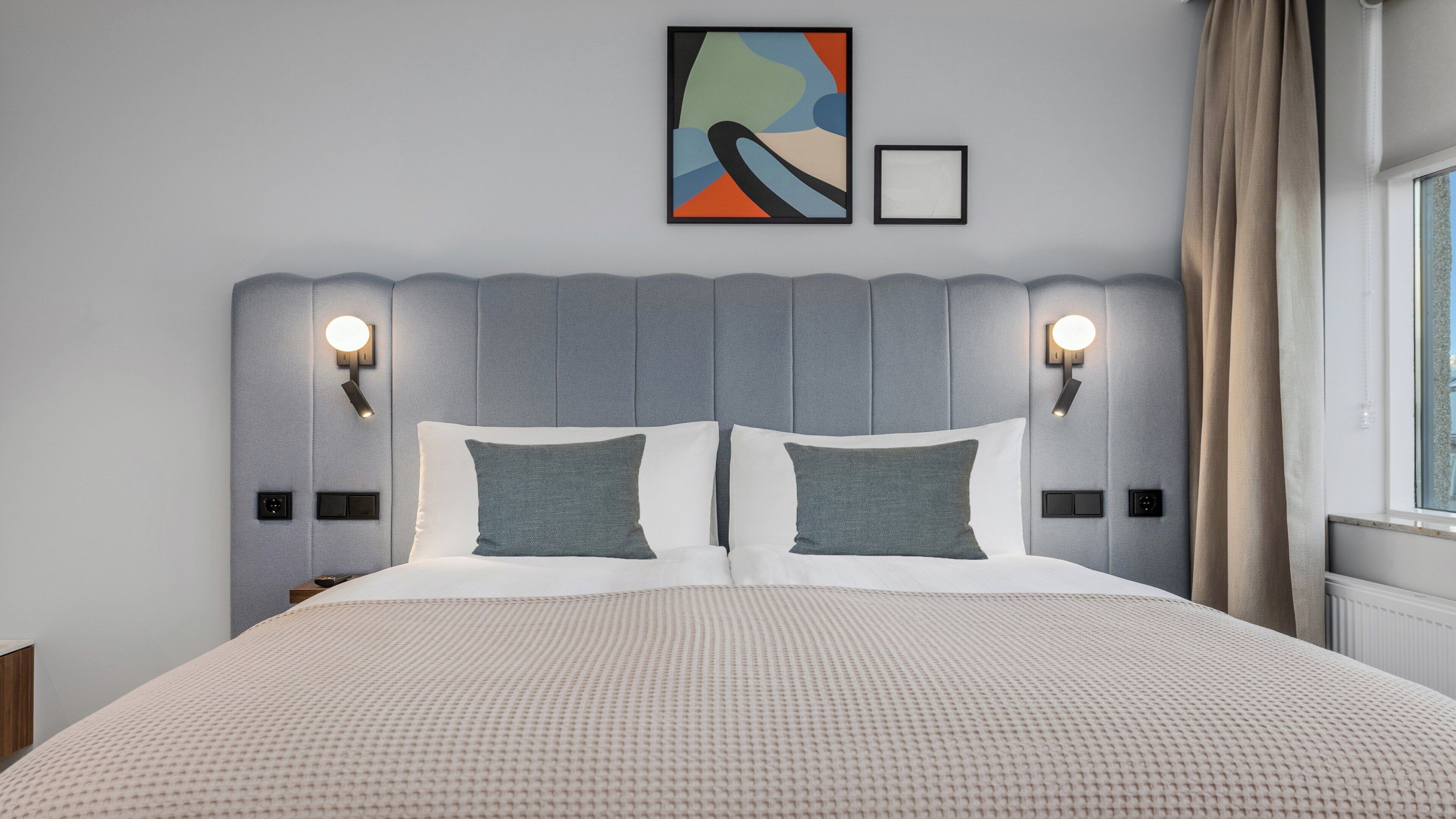 Une chambre d’hôtel moderne avec un grand lit, deux tables de chevet et un tableau abstrait accroché au mur.