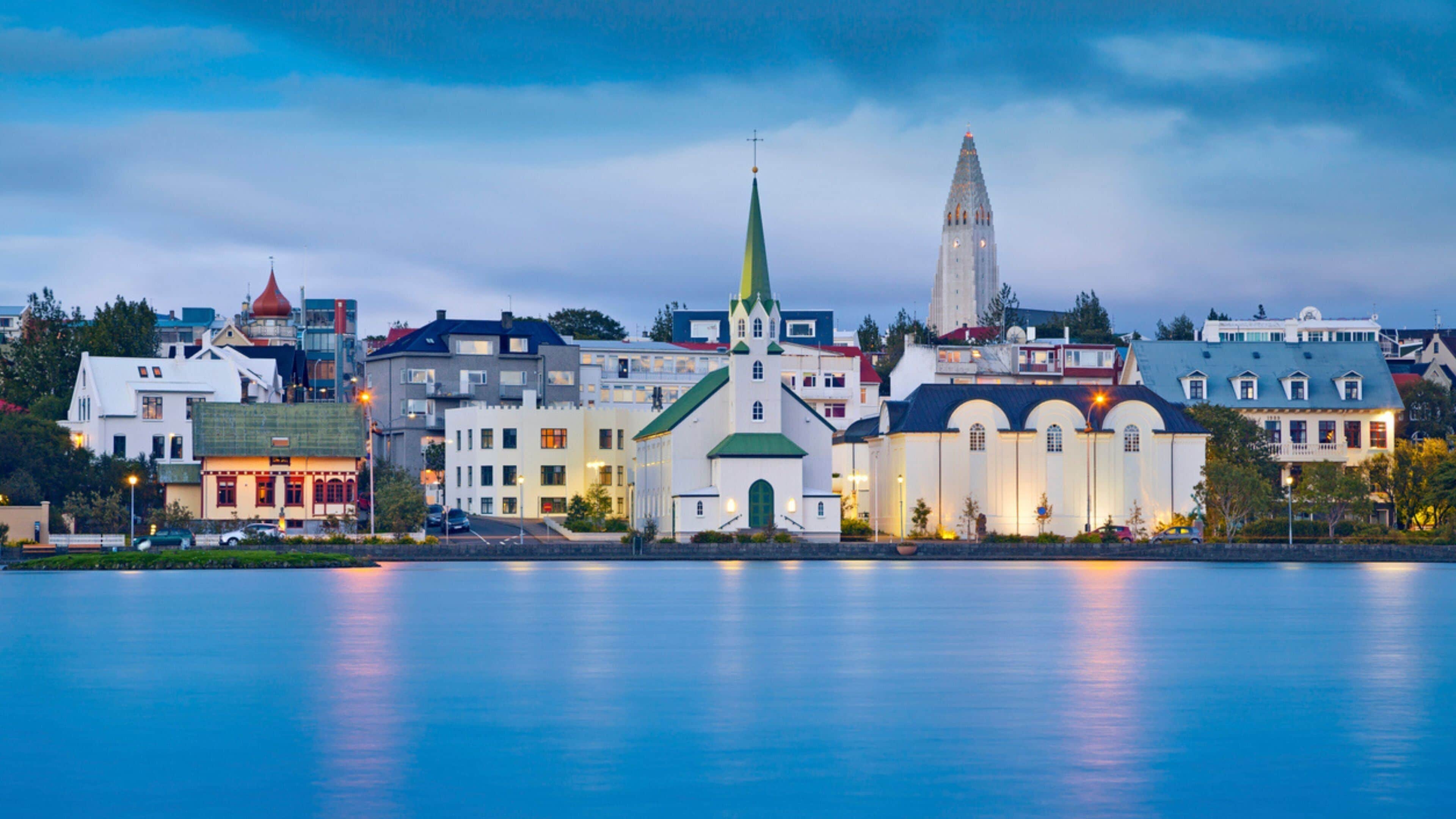 A waterfront cityscape with a prominent church, a tall tower, and various buildings along the shore.