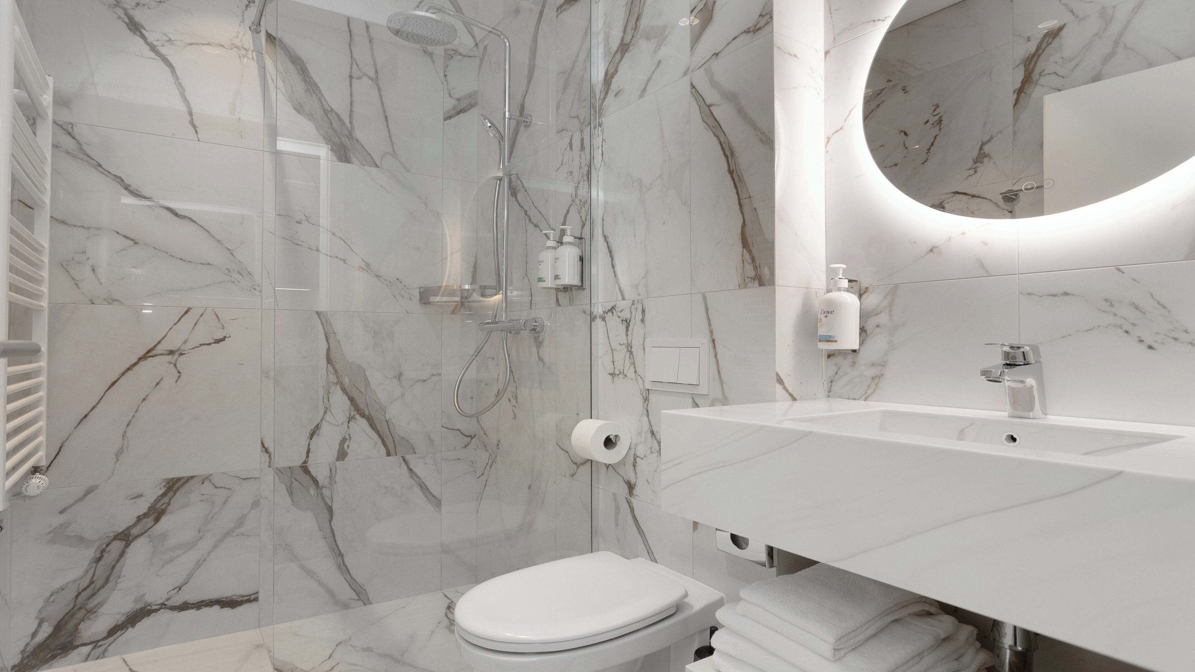 A modern bathroom with a marble backsplash, a glass-enclosed shower, a white sink, and a toilet.