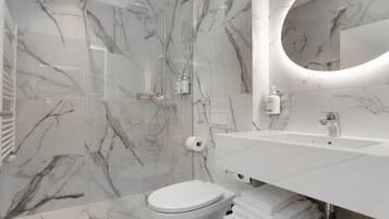 A modern bathroom with a marble backsplash, a glass-enclosed shower, a white sink, and a toilet.