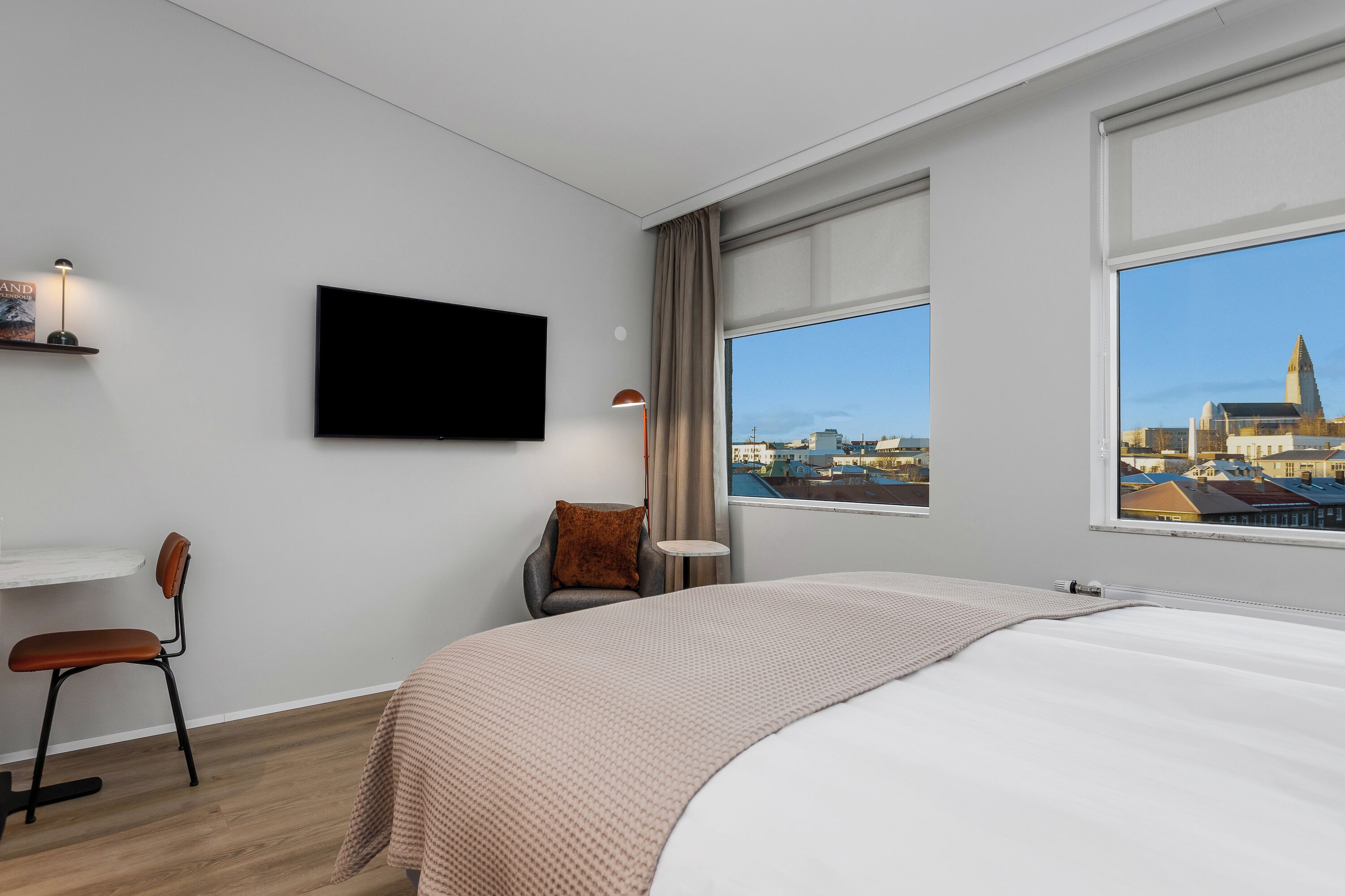 Een moderne hotelkamer met een groot bed, een flatscreen-tv, een bureau met stoel, en uitzicht op een stadsgezicht door grote ramen.