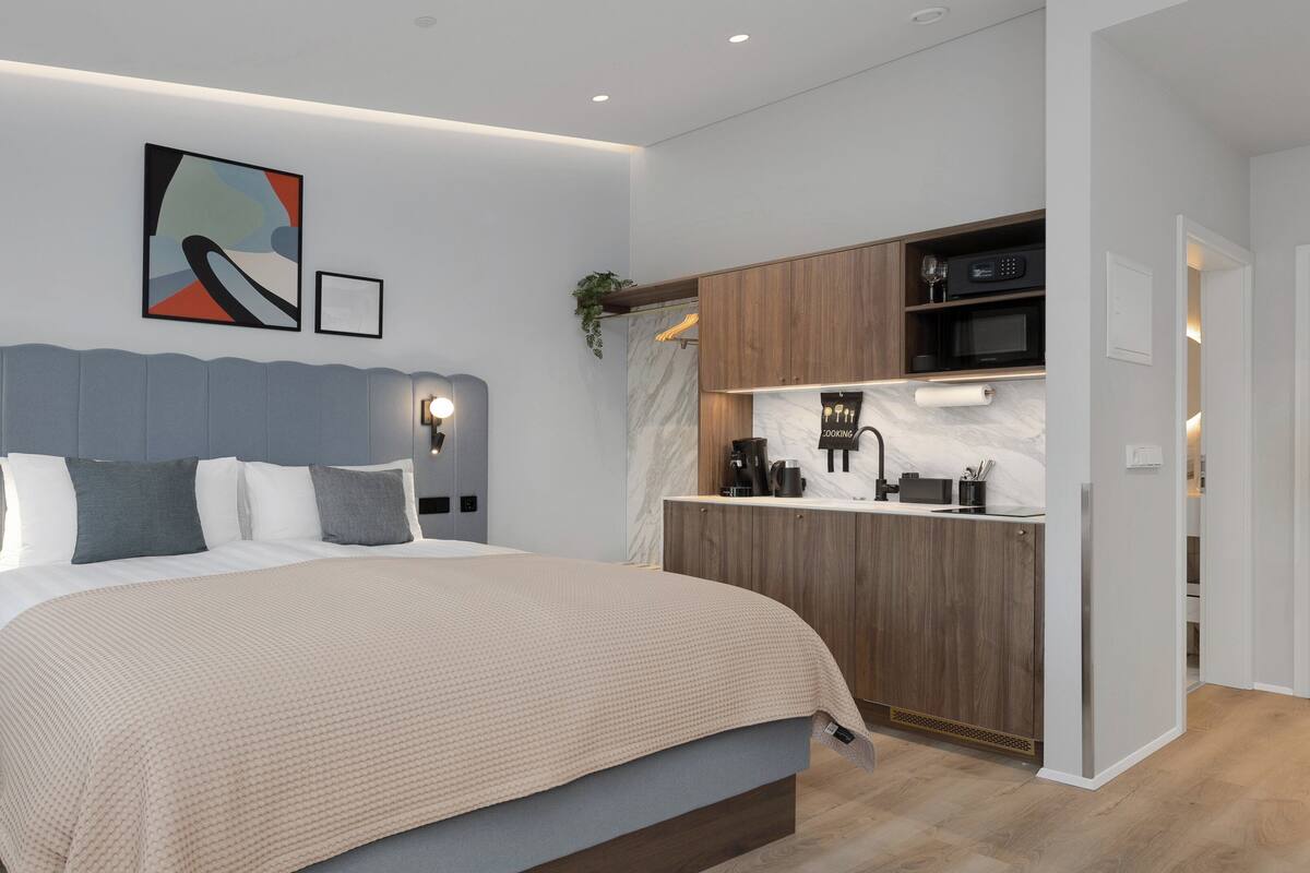 Un dormitorio moderno con una cama grande, un escritorio empotrado y una zona de cocina.