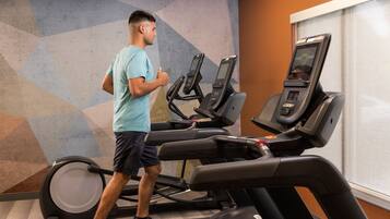 Une personne utilise un tapis de course dans une salle de sport. Le mur est décoré de motifs géométriques et une fenêtre est dotée de stores.