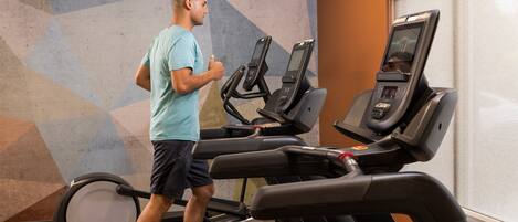 A person using a treadmill in a gym with a geometric wall design and a window with blinds.