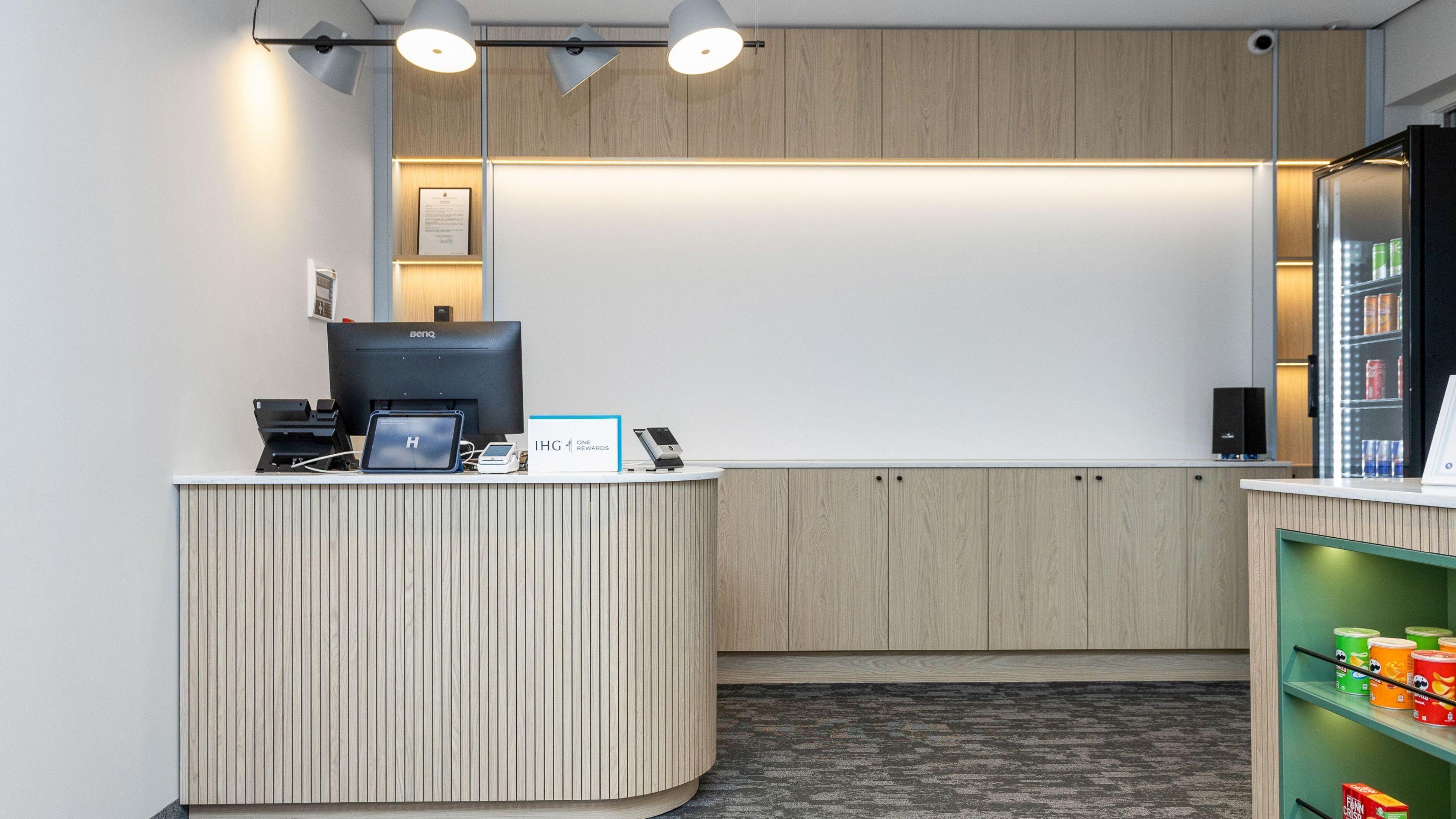 A reception desk with a BenQ monitor, a printer, and a sign for IHG One Rewards.