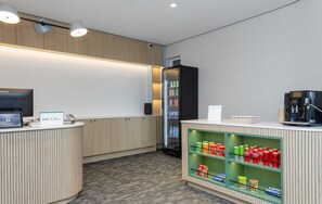 Zona de recepción con mostrador, refrigerador, máquina de café y estante para bebidas.