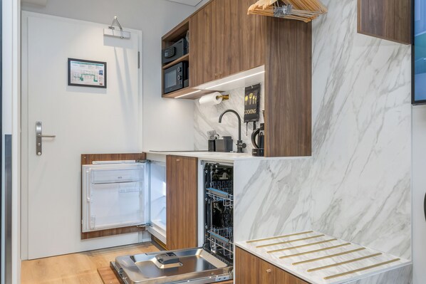 A compact kitchen with a built-in dishwasher, wooden cabinets, and a marble backsplash.