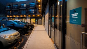 Un bâtiment moderne, sur lequel on peut lire l’enseigne « Central Lofts Queenstown, unité 9 », doté d’une entrée en verre et d’un espace de stationnement où sont garées plusieurs voitures.