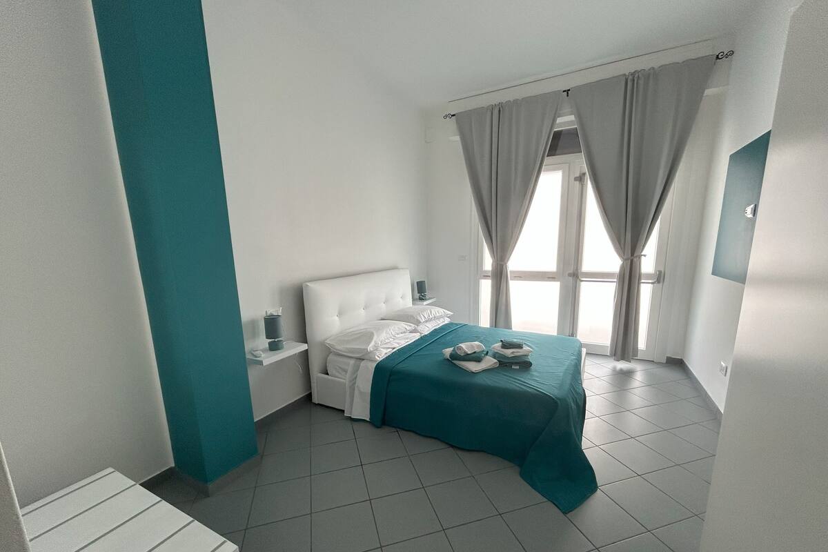Een moderne hotelkamer met een net opgemaakt bed, een nachtkastje en een raam met gordijnen.