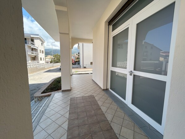 A corridor with a tiled floor, a glass door, and a view of a residential area with buildings and a street.