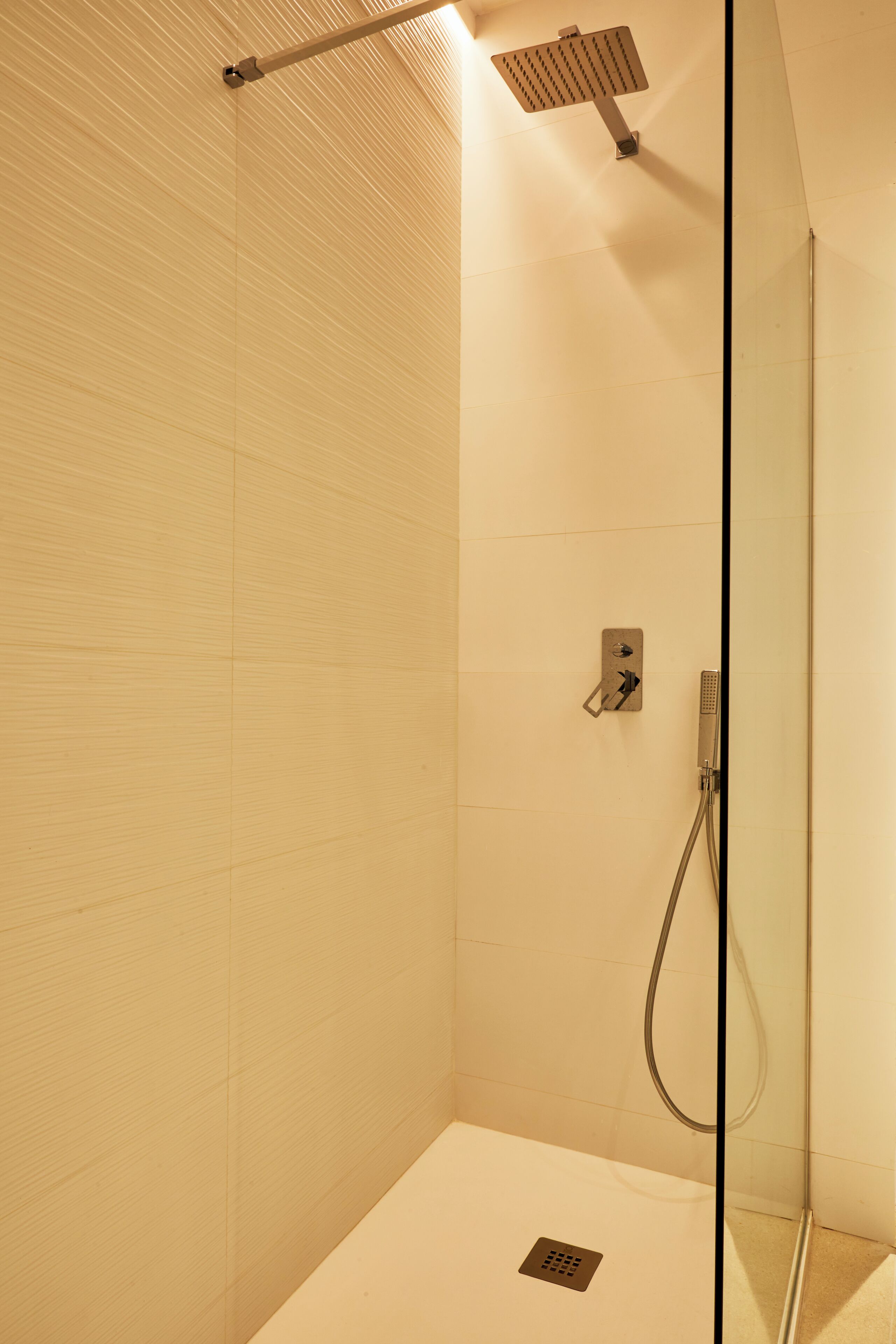 Une douche moderne dotée d’une paroi en verre, d’un pommeau de douche à main et d’un panneau de commande fixé au mur.