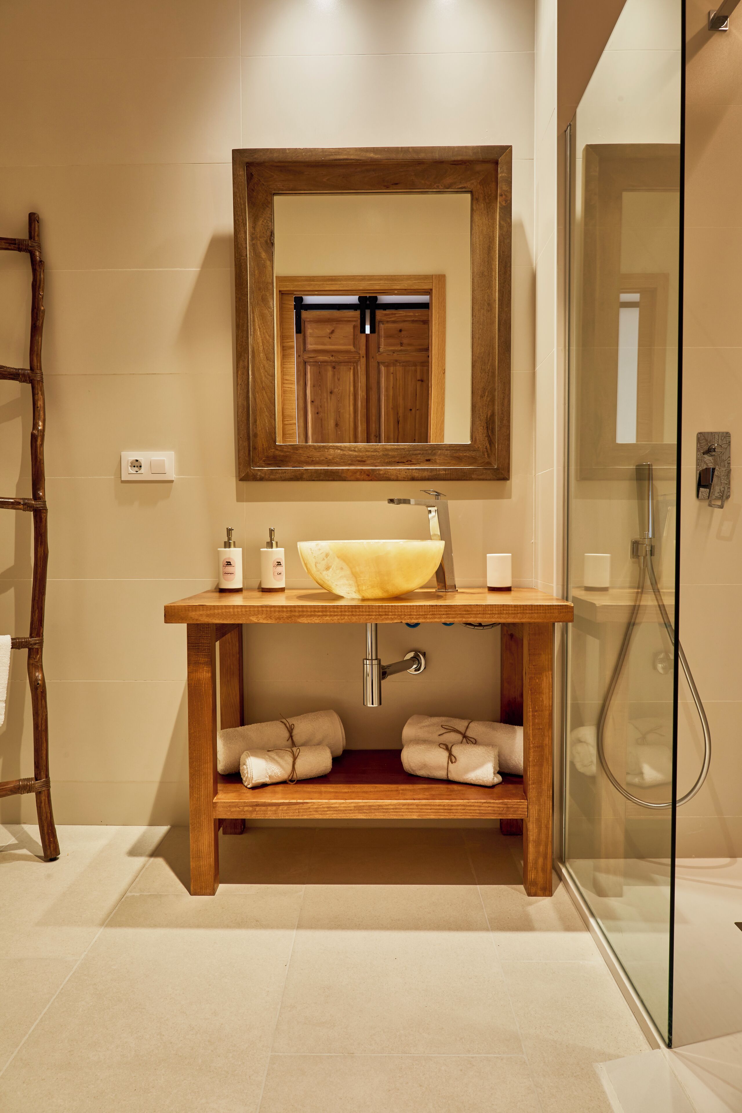Une salle de bain avec un meuble-lavabo en bois, un grand miroir, une cabine de douche en verre et un porte-serviettes.