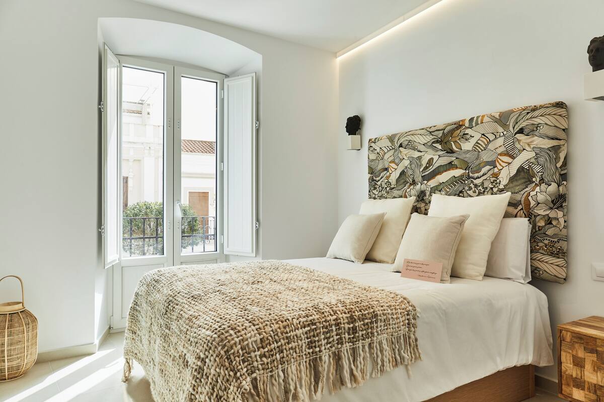 A bedroom with a large bed, a woven throw blanket, and a view of the outside through an open door.