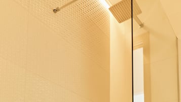 A modern bathroom with a glass shower enclosure, a visible drain, and a tiled wall.