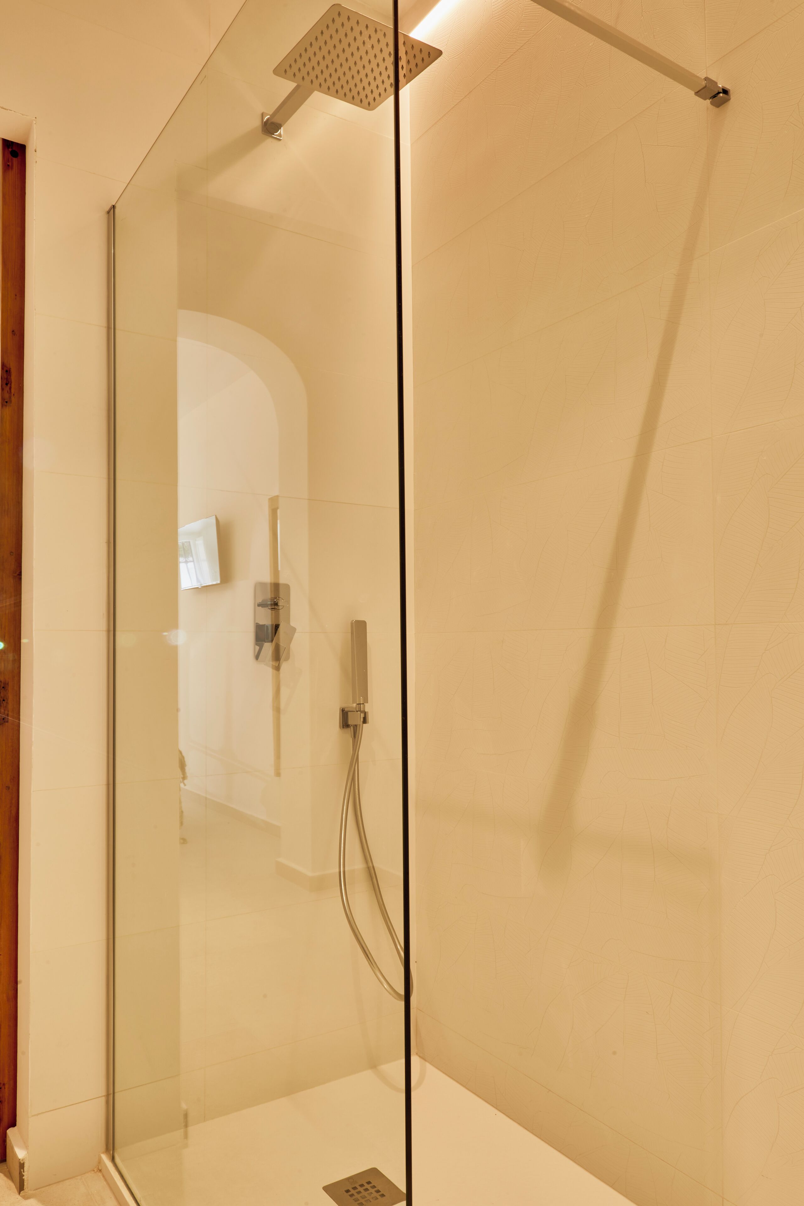 A glass-enclosed shower with a handheld showerhead and a wall-mounted control panel.