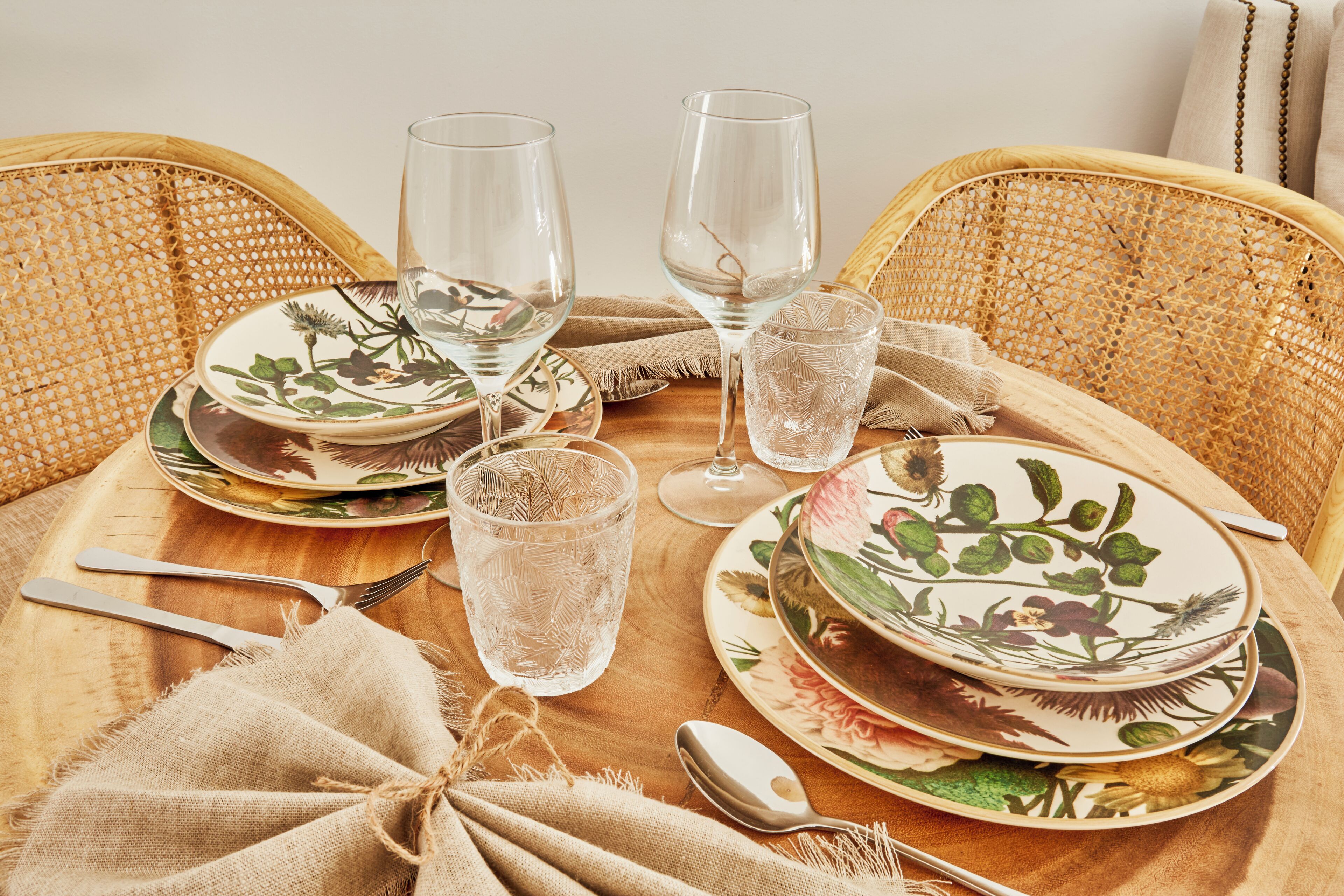 Una mesa de comedor dispuesta con platos de estampado floral, vasos transparentes y cubiertos.