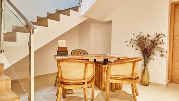 A modern dining area with a wooden table and chairs, a vase with dried plants, and a staircase in the background.