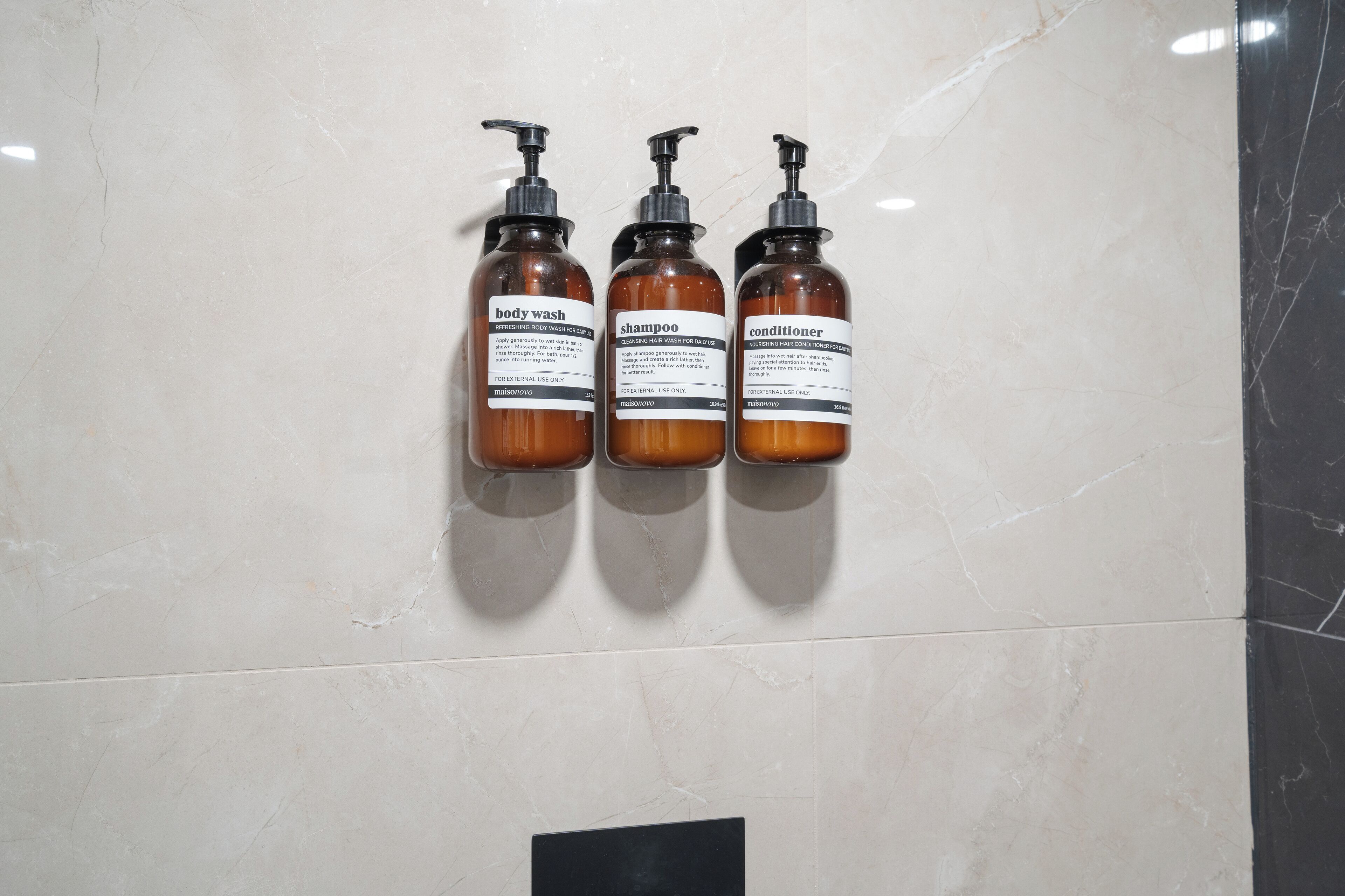 Drie flessen douchegel, shampoo en conditioner op een muur.