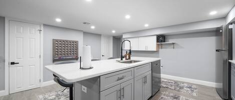 Una cocina moderna con armarios grises, encimera blanca y refrigerador de acero inoxidable.