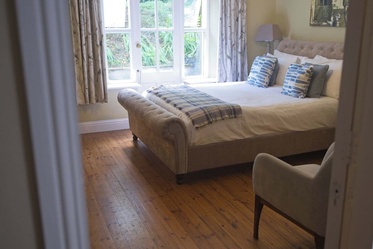A bedroom with a large bed, a chair, and a window with curtains.