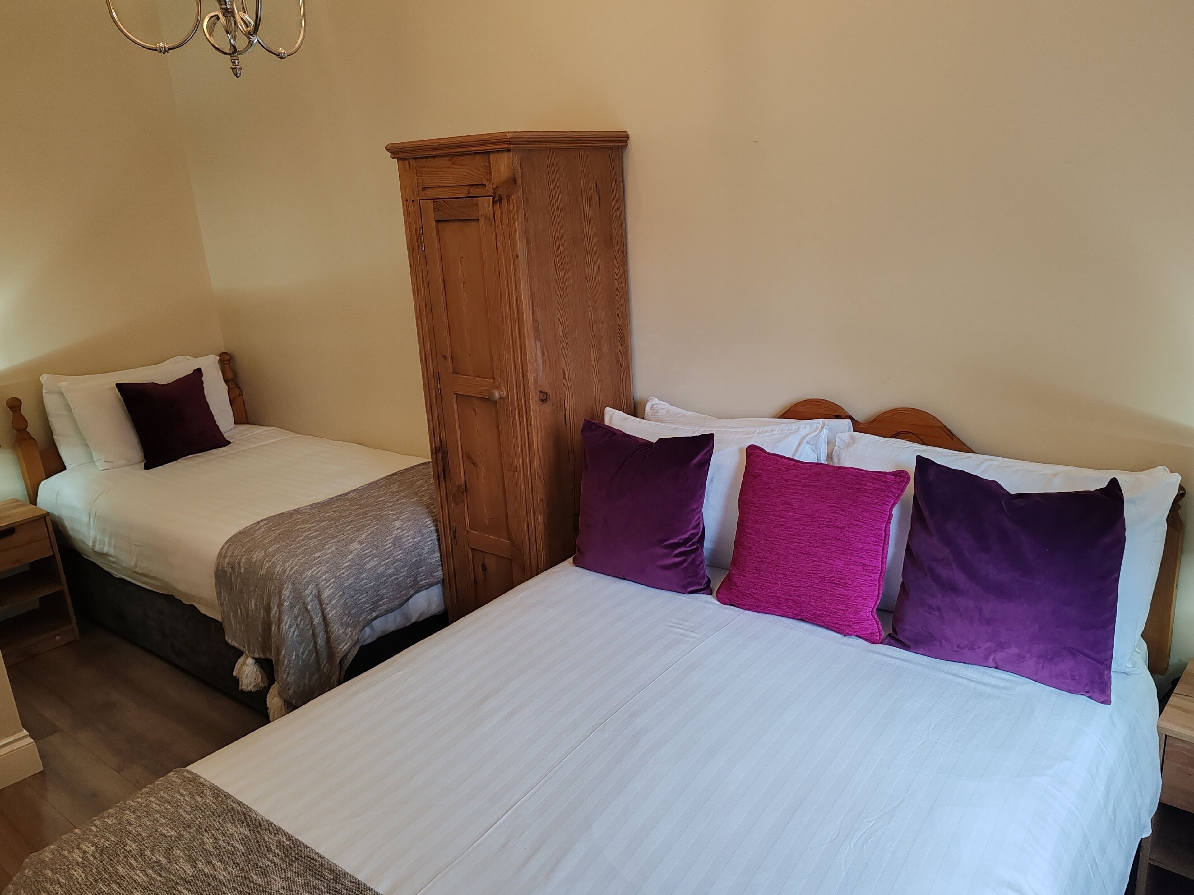 Een slaapkamer met twee bedden, een houten garderobe en een kroonluchter.
