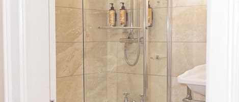 Eine begegnete Dusche mit Handbrause und Wandarmatur. Auf einem Regal befinden sich zwei Shampooflaschen und ein Seifenspender.