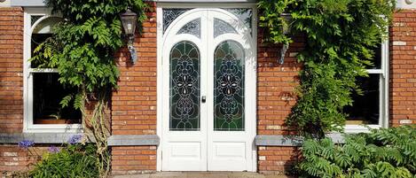Una casa de ladrillo con una puerta blanca, dos ventanas arqueadas y una puerta de vidrio decorativa.