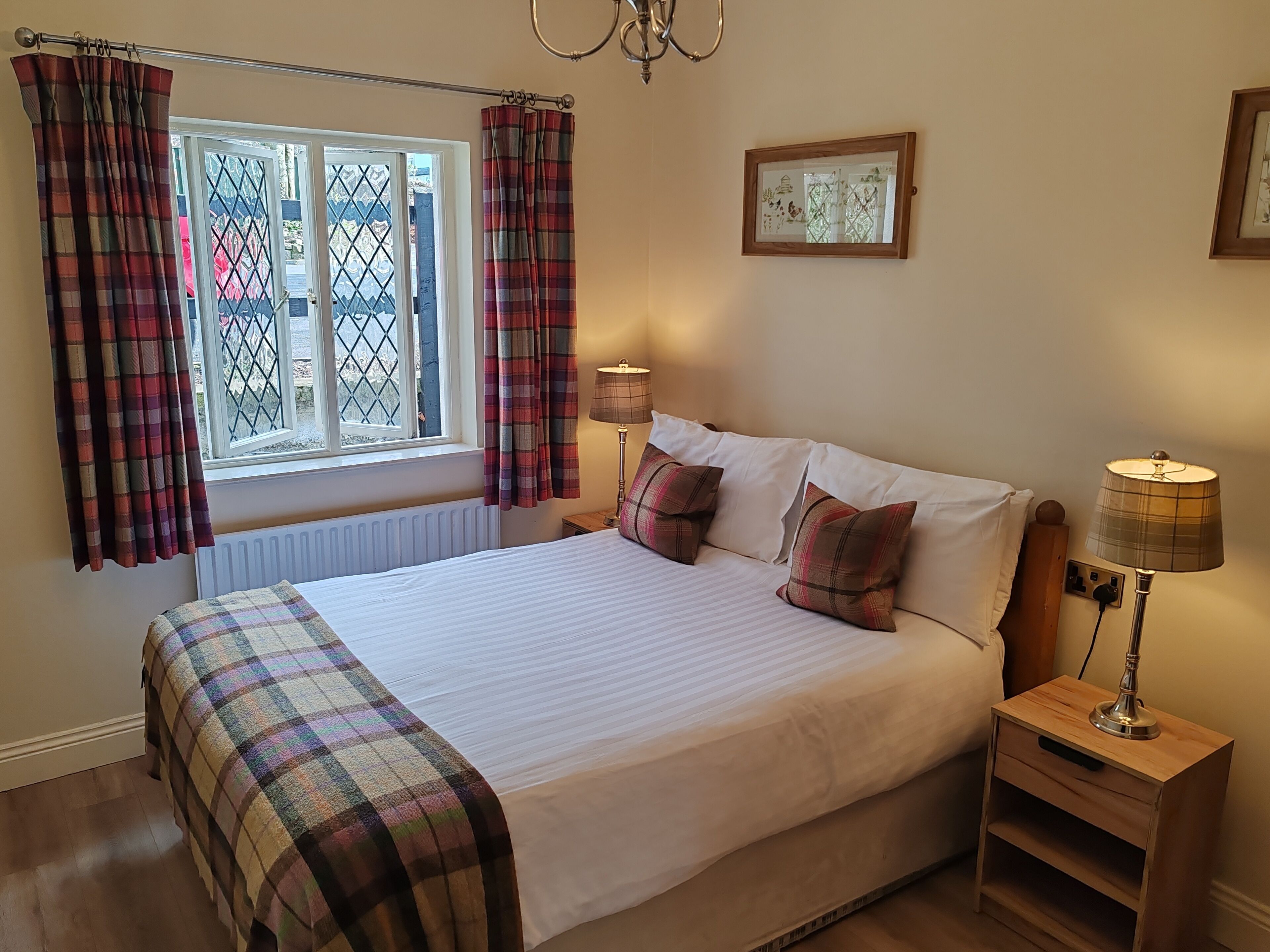 A neatly made bed with plaid bedding, a bedside lamp, and a window with curtains.