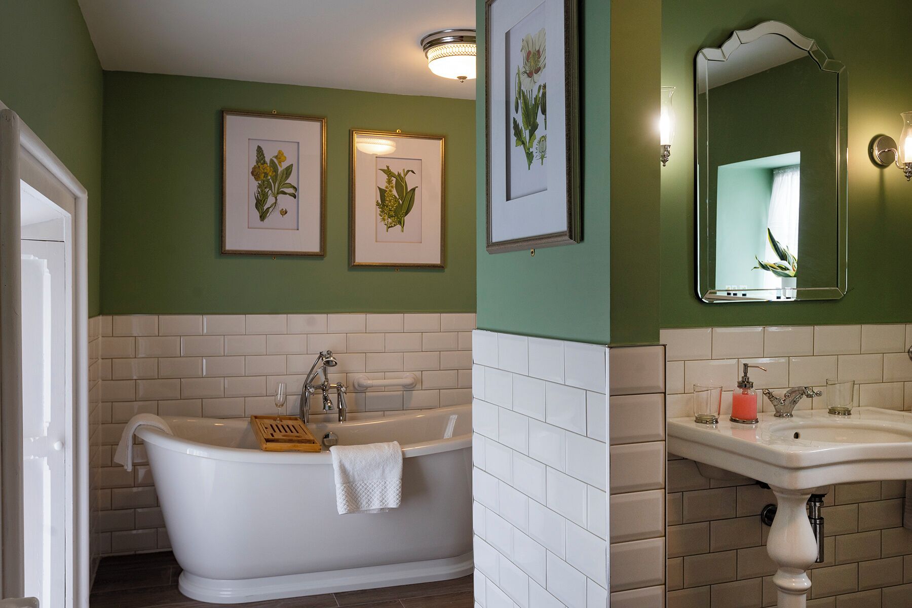 A bathroom with a freestanding bathtub, a sink, and two framed botanical prints on the wall.