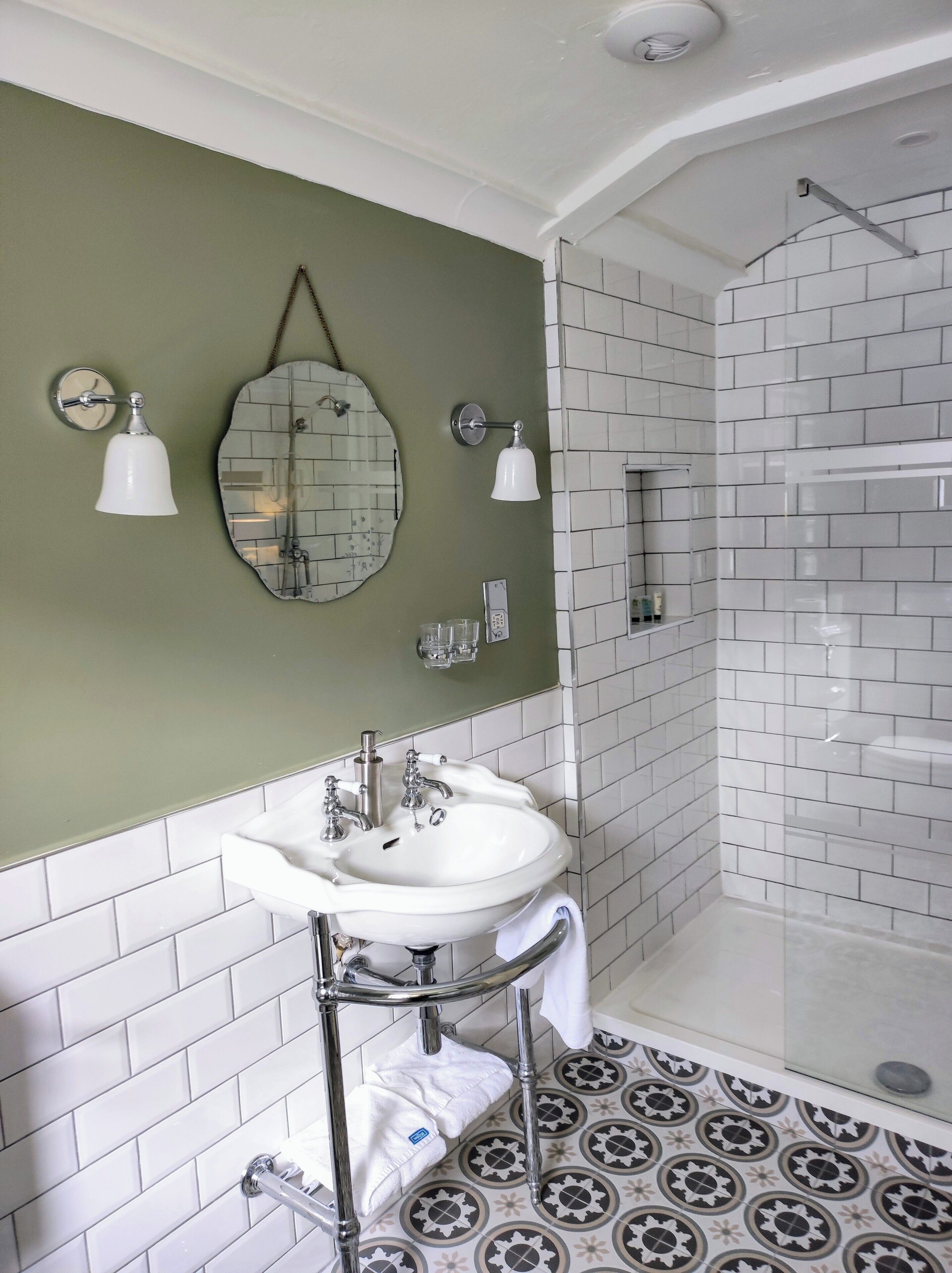 Un baño con lavamanos blanco, paredes verdes y piso estampado.